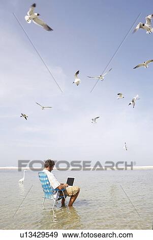Stock Photo - Man sitting in ocean surf with laptop. Fotosearch