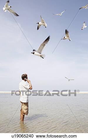 Stock Image - Man talking on cell phone in middle of water. Fotosearch