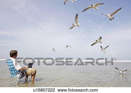 Stock Image - Man using laptop in middle of water. Fotosearch