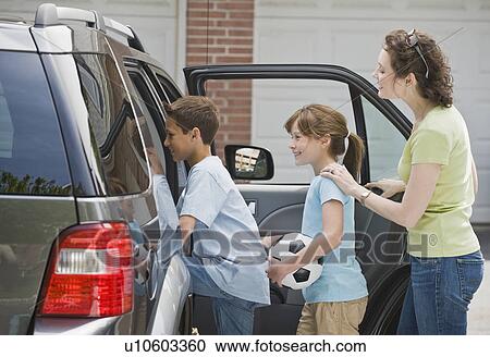 Stock Image - Mother and children getting into car with soccer ball. Fotosearch