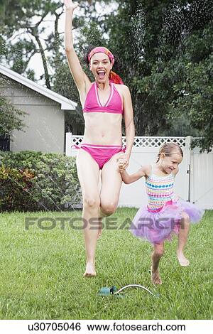 Stock Photograph - Mother and daughter running through sprinkler. Fotosearch
