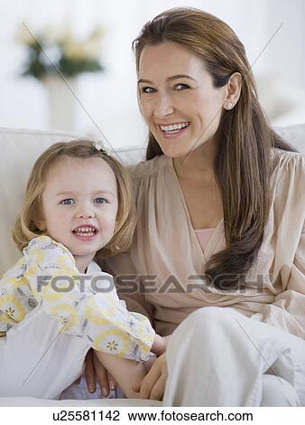 Stock Image - Mother and daughter sitting on sofa. Fotosearch