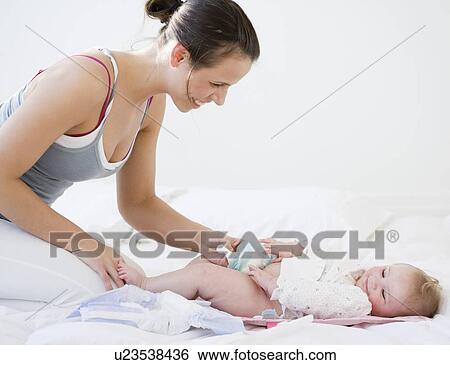 Stock Photograph - Mother changing baby’s diaper. Fotosearch