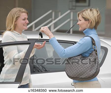 Stock Image - Mother handing car keys to teenaged daughter. Fotosearch