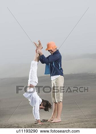 Stock Image - Mother holding daughter upside down on beach. Fotosearch