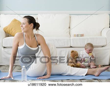 Stock Image - Mother practicing yoga next to baby on floor. Fotosearch