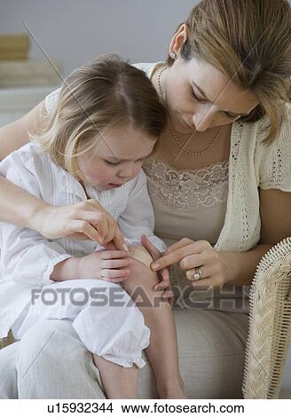 Picture - Mother putting bandage on daughter’s knee. Fotosearch