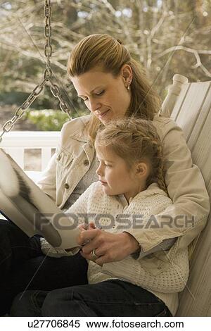 Stock Photography - Mother reading to daughter on porch swing. Fotosearch