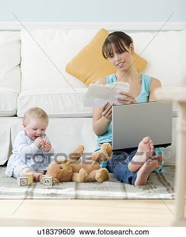 Stock Photo - Mother working next to baby playing on floor. Fotosearch