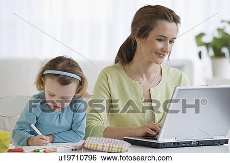 Stock Photograph - Mother working next to daughter coloring. Fotosearch