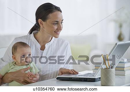 Mother working on laptop and holding baby son View Large Photo Image Stock Image - Mother working on laptop and holding baby son. Fotosearch