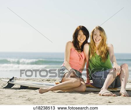 Stock Image - Multi-ethnic women sitting on surf board. Fotosearch