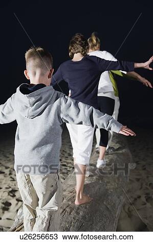 Stock Image - Parents, daughter, and son balancing on driftwood. Fotosearch