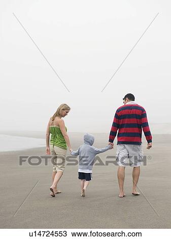 Stock Image - Parents holding hands with son on beach. Fotosearch