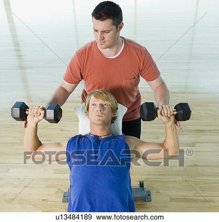 Personal trainer spotting man with dumbbells View Large Photo Image Stock Photo - Personal trainer spotting man with dumbbells. Fotosearch