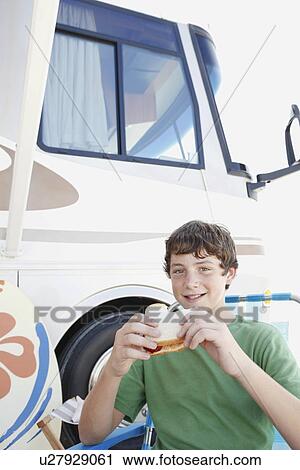Stock Image - Portrait of boy eating sandwich outside motor home. Fotosearch