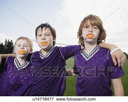 Stock Photo - Portrait of boys in soccer uniforms with orange wedges in mouth. Fotosearch
