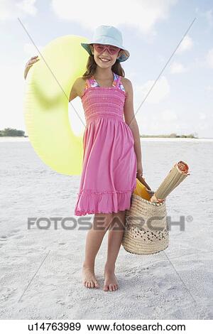Stock Photo - Portrait of girl holding inflatable tube and bag on beach. Fotosearch