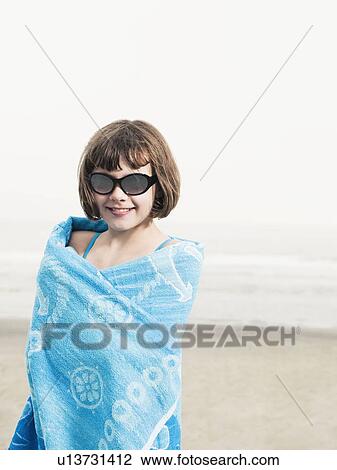 Stock Image - Portrait of girl in sunglasses wrapped in a towel on beach. Fotosearch