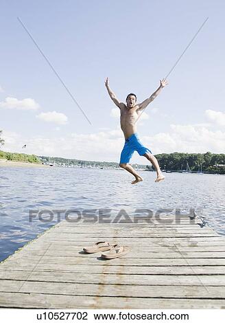 Stock Image - Portrait of man jumping off dock into lake. Fotosearch