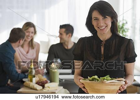 Portrait of woman holding salad bowl with friends in background View Large Photo Image Picture - Portrait of woman holding salad bowl with friends in background. Fotosearch