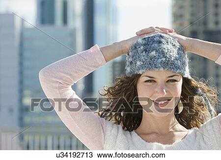 Stock Image - Portrait of woman in stocking cap with city in background. Fotosearch