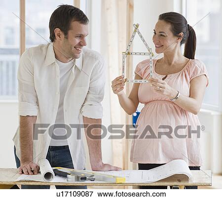 Pregnant Hispanic couple looking at ruler shaped like house View Large Photo Image Stock Photo - Pregnant Hispanic couple looking at ruler shaped like house. Fotosearch