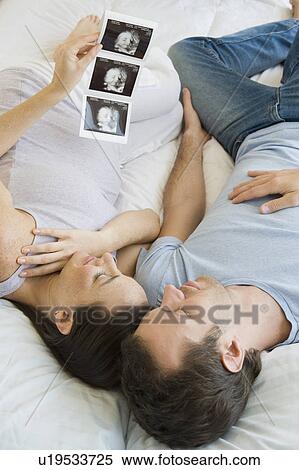Stock Photography - Pregnant Hispanic couple looking at ultrasound printout. Fotosearch