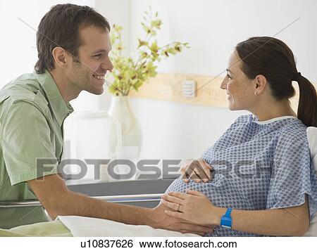 Stock Photograph - Pregnant Hispanic couple smiling at each other. Fotosearch