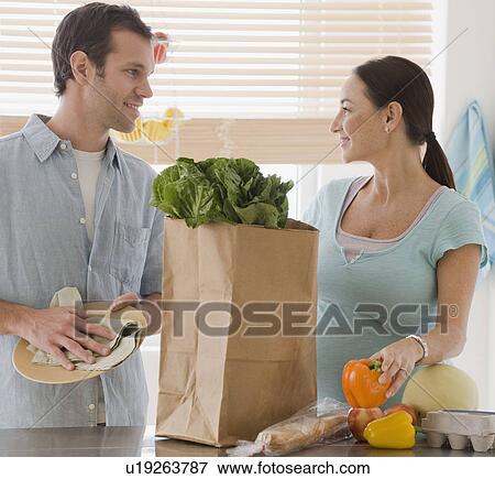 Stock Photo - Pregnant Hispanic couple unpacking groceries. Fotosearch