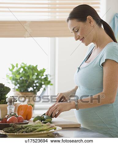 Picture - Pregnant Hispanic woman chopping vegetables. Fotosearch