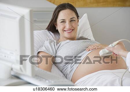 Stock Image - Pregnant Hispanic woman looking at ultrasound monitor. Fotosearch