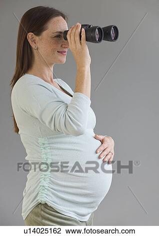 Stock Image - Pregnant Hispanic woman looking through binoculars. Fotosearch