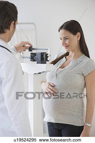 Stock Photography - Pregnant Hispanic woman on scale in doctor’s office. Fotosearch