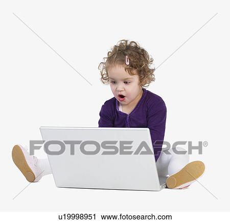 Stock Image - Preschool girl playing with laptop. Fotosearch