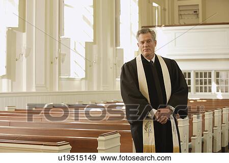 Stock Photo - Priest standing next to pews. Fotosearch