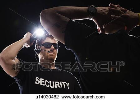 Stock Image - Security guard shining flashlight on man. Fotosearch