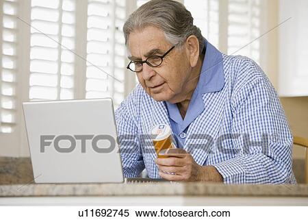 Stock Photography - Senior man with medication bottle looking at laptop. Fotosearch