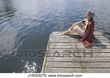 Stock Photo - Senior woman sitting on dock. Fotosearch