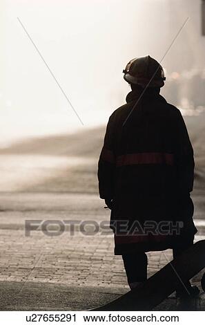 Stock Image - Silhouette of fireman looking at smoke in distance. Fotosearch