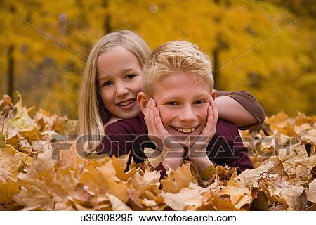 Stock Photography - Sister and brother laying in autumn leaves. Fotosearch