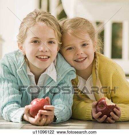 Stock Image - Sisters eating apple on porch. Fotosearch