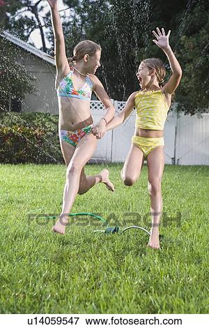 Stock Photo - Sisters in bathing suits running through sprinkler. Fotosearch