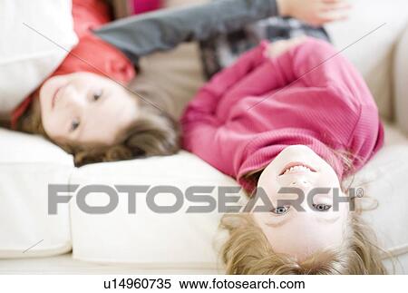 Stock Photography - Sisters laying on sofa. Fotosearch