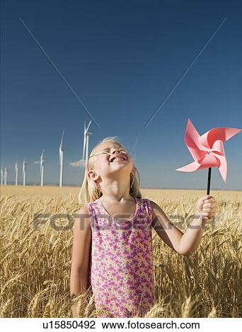 Stock Image - Smiling girl holding pinwheel on wind farm. Fotosearch