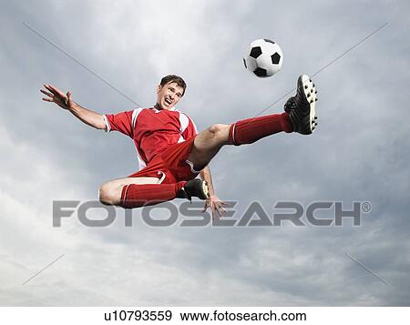 Stock Photo - Soccer player kicking soccer ball in mid-air. Fotosearch