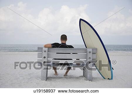 Surfer sitting on bench next to surfboard View Large Photo Image Stock Photo - Surfer sitting on bench next to surfboard. Fotosearch