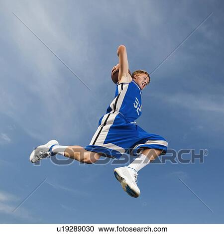 Stock Image - Teenage basketball player in mid-air throwing basketball. Fotosearch