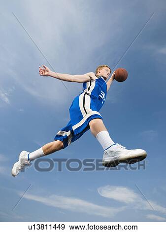 Stock Photo - Teenage basketball player in mid-air with basketball. Fotosearch