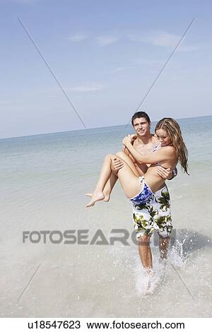 Stock Image - Teenage boy carrying girlfriend in ocean. Fotosearch